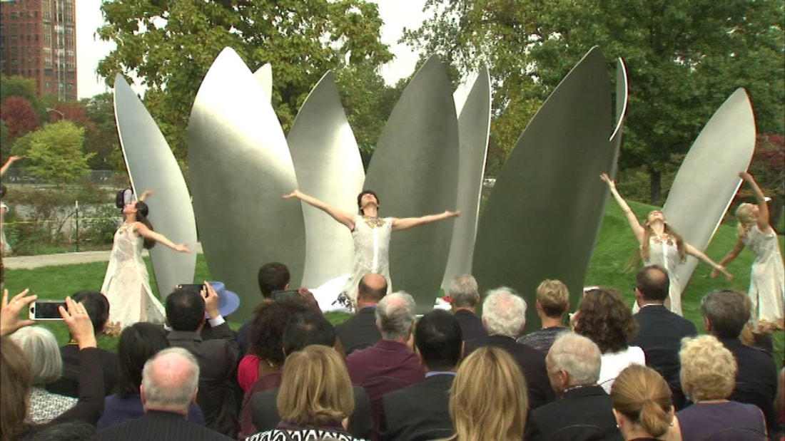 Dancers stand in front of the sculpture with audience in front